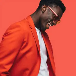 Man laughing and wearing an orange jacket on an orange background