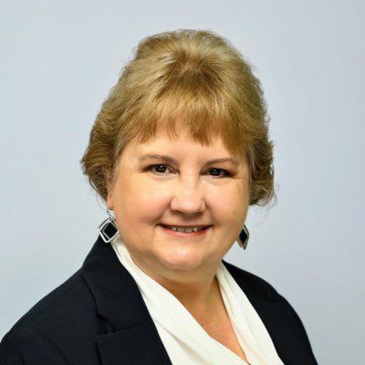 Woman with short, light brown hair wearing a black blazer and white blouse, smiling confidently against a plain background, embodies the spirit of digital-led customer success.